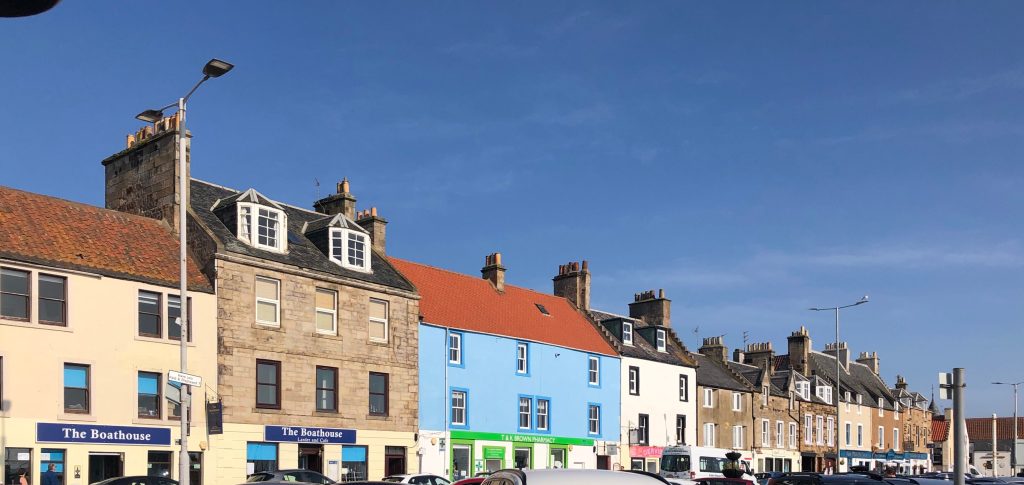 Charming view of Anstruther waterfront, featuring colorful fishing boats docked along the quay, quaint stone buildings, and the sparkling sea. A picturesque spot for visitors exploring Scotland’s East Neuk fishing villages.